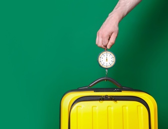 Man weighing stylish suitcase against color background, closeup. Space for text