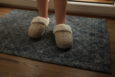 Photo of Woman wearing warm beige slippers on wooden floor, closeup