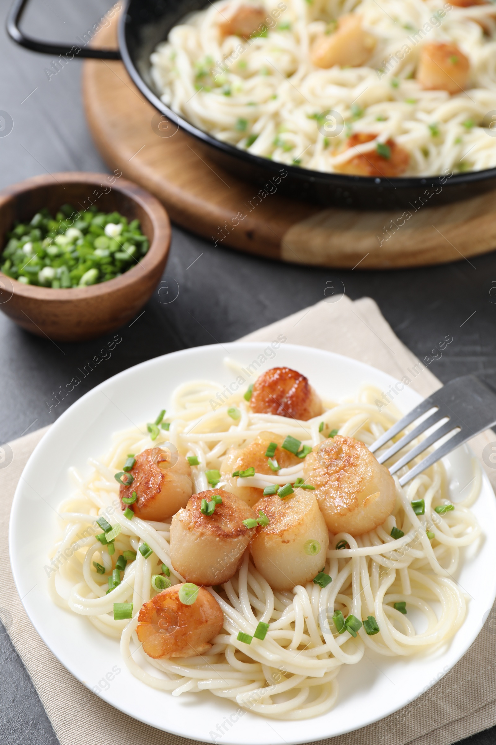 Photo of Delicious scallop pasta with green onion served on grey table