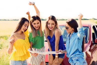 Photo of Happy beautiful young women with map standing near car in countryside