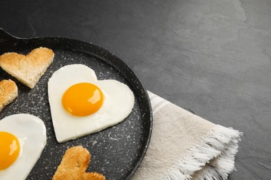 Photo of Heart shaped fried eggs and toasts in frying pan on grey table, closeup. Space for text