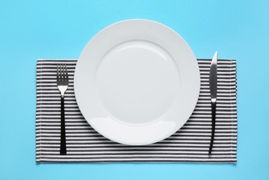 Photo of Clean plate and shiny silver cutlery on light blue background, flat lay