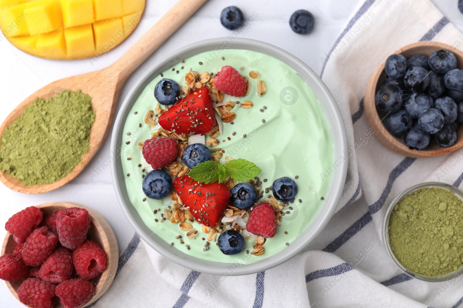 Photo of Tasty matcha smoothie bowl served with berries and oatmeal on white tiled table, flat lay. Healthy breakfast