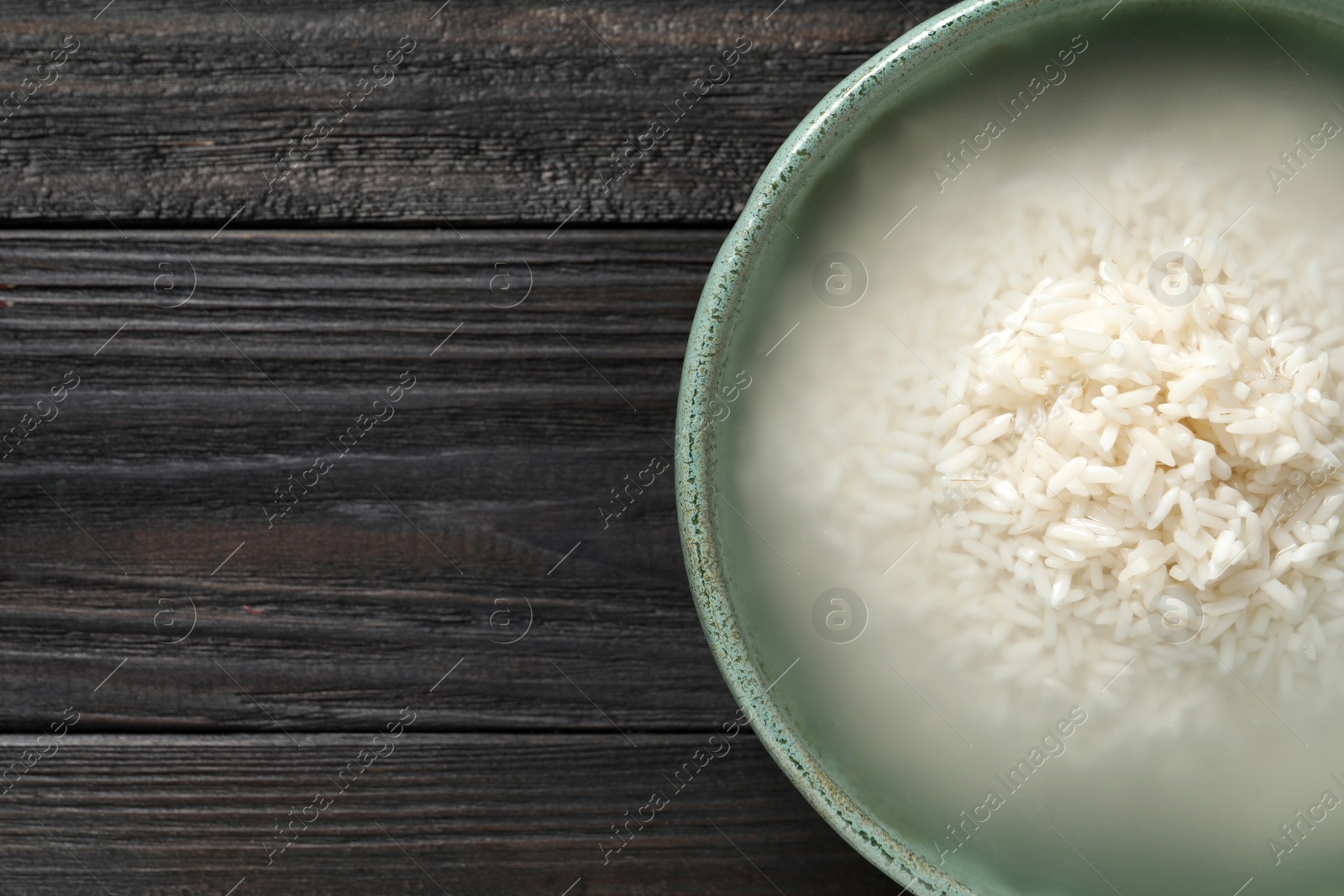 Photo of Bowl with rice soaked in water on black wooden table, top view. Space for text