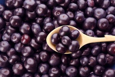 Photo of Wooden spoon and fresh ripe acai berries as background, closeup