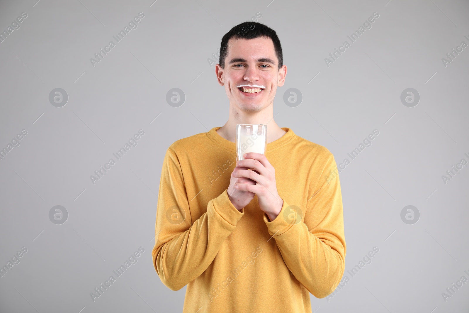 Photo of Happy man with milk mustache holding glass of tasty dairy drink on gray background