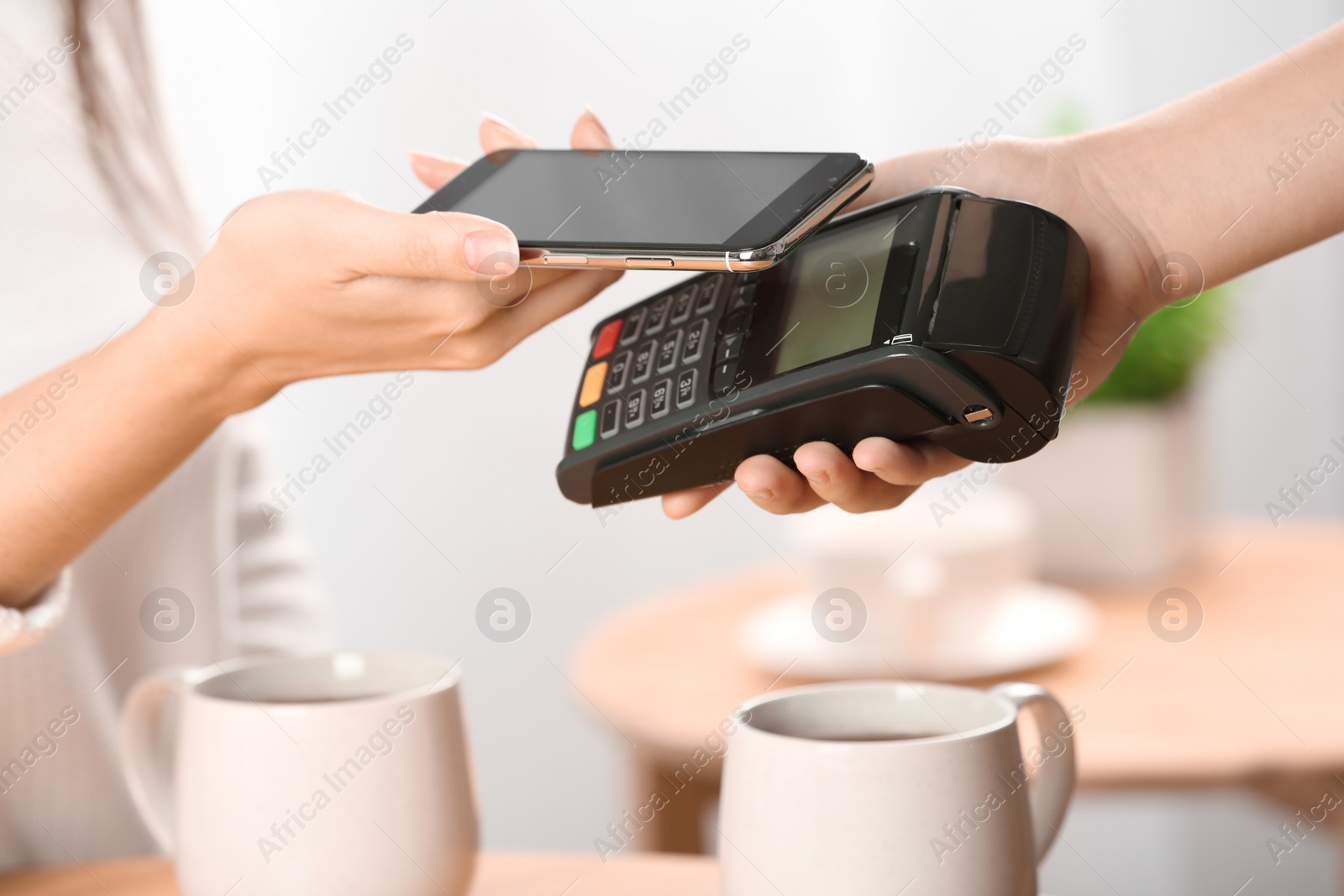 Photo of Woman using terminal for contactless payment with smartphone in cafe