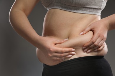 Woman touching belly fat on grey background, closeup. Overweight problem