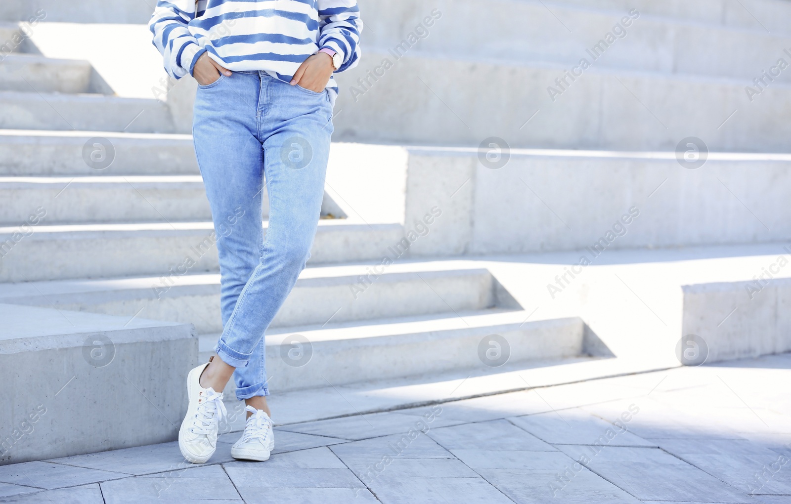 Photo of Young hipster woman in stylish jeans standing near stairs outdoors