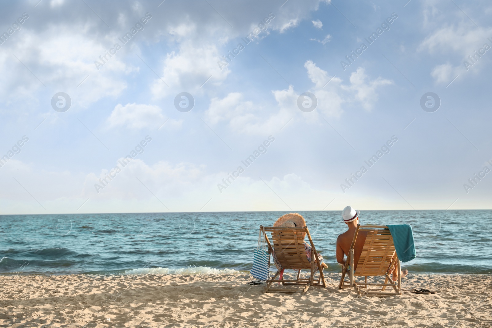 Photo of Young couple relaxing in deck chairs on beach near sea