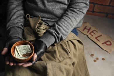 Poor homeless man holding bowl with donations on floor, closeup