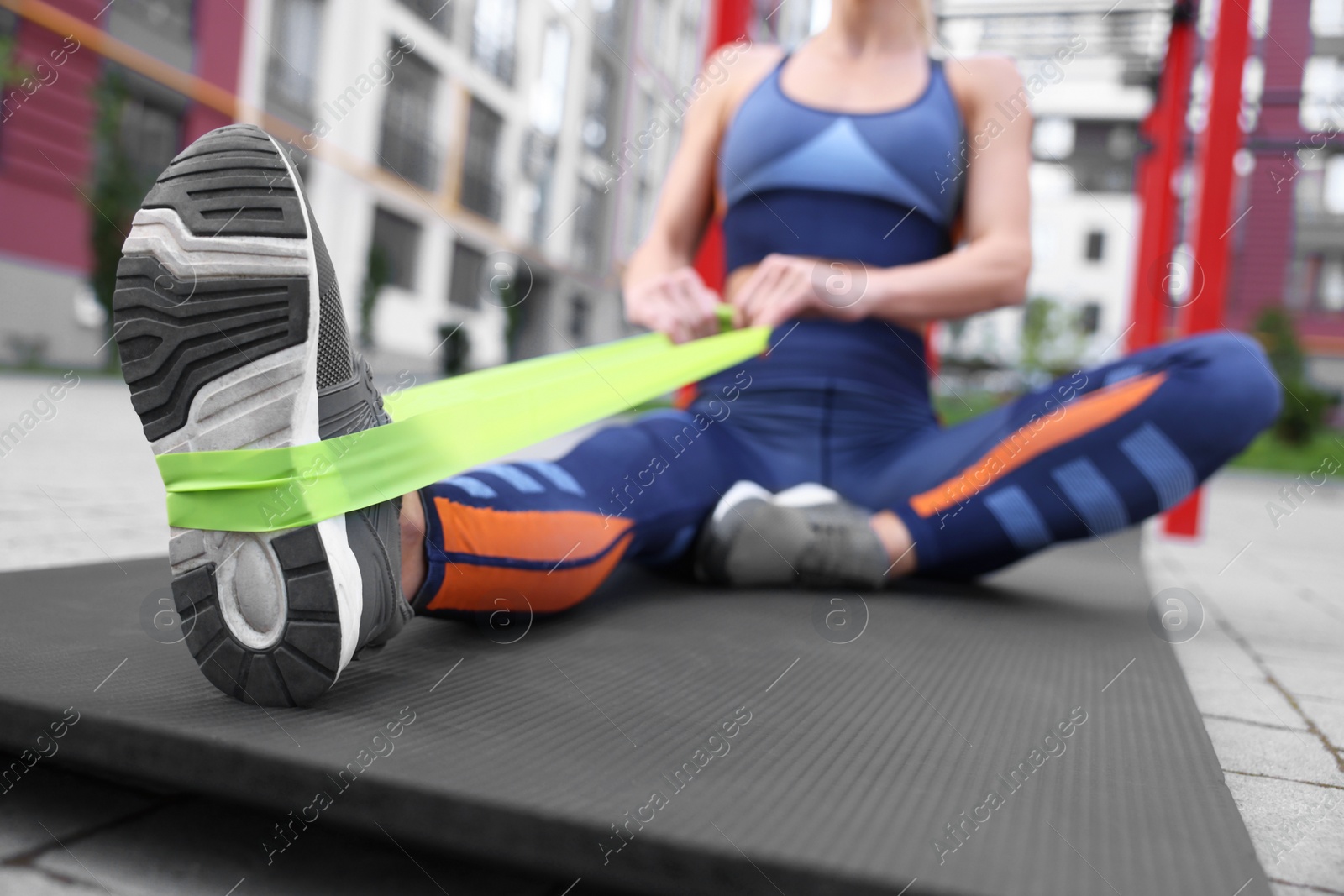 Photo of Woman doing exercise with fitness elastic band on mat outdoors, closeup