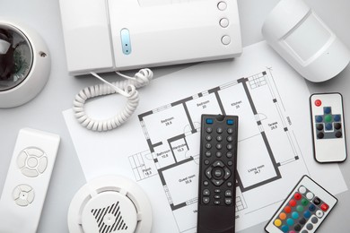 Photo of Remote controls, intercom, building plan, smoke and movement detectors on white background, flat lay. Home security system