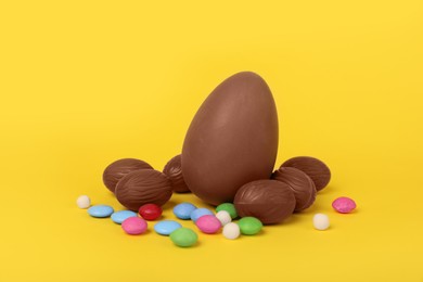 Delicious chocolate eggs and colorful candies on yellow background, closeup