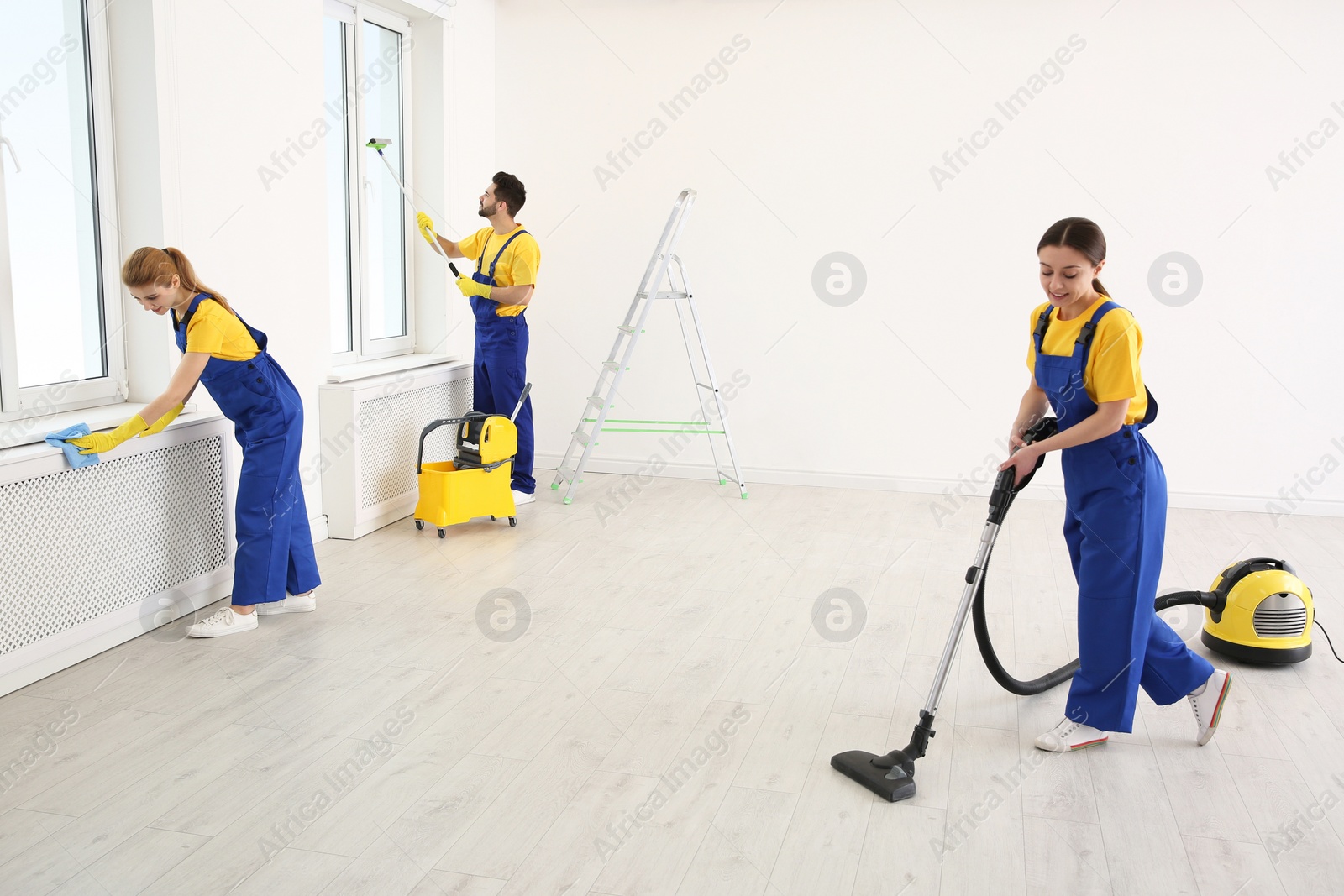 Photo of Team of professional janitors in uniforms cleaning room