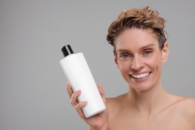 Washing hair. Portrait of beautiful happy woman with bottle on light grey background, space for text