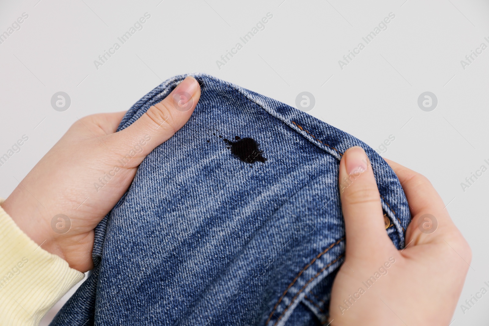 Photo of Woman holding jeans with black ink stain on light grey background, closeup