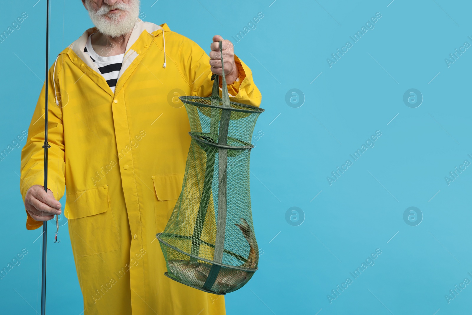 Photo of Fisherman holding rod and fishing net with catch on light blue background, closeup. Space for text