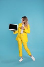 Young woman with modern laptop on light blue background