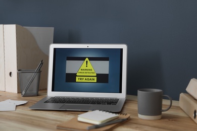 Photo of Laptop with warning about virus attack on wooden table in office
