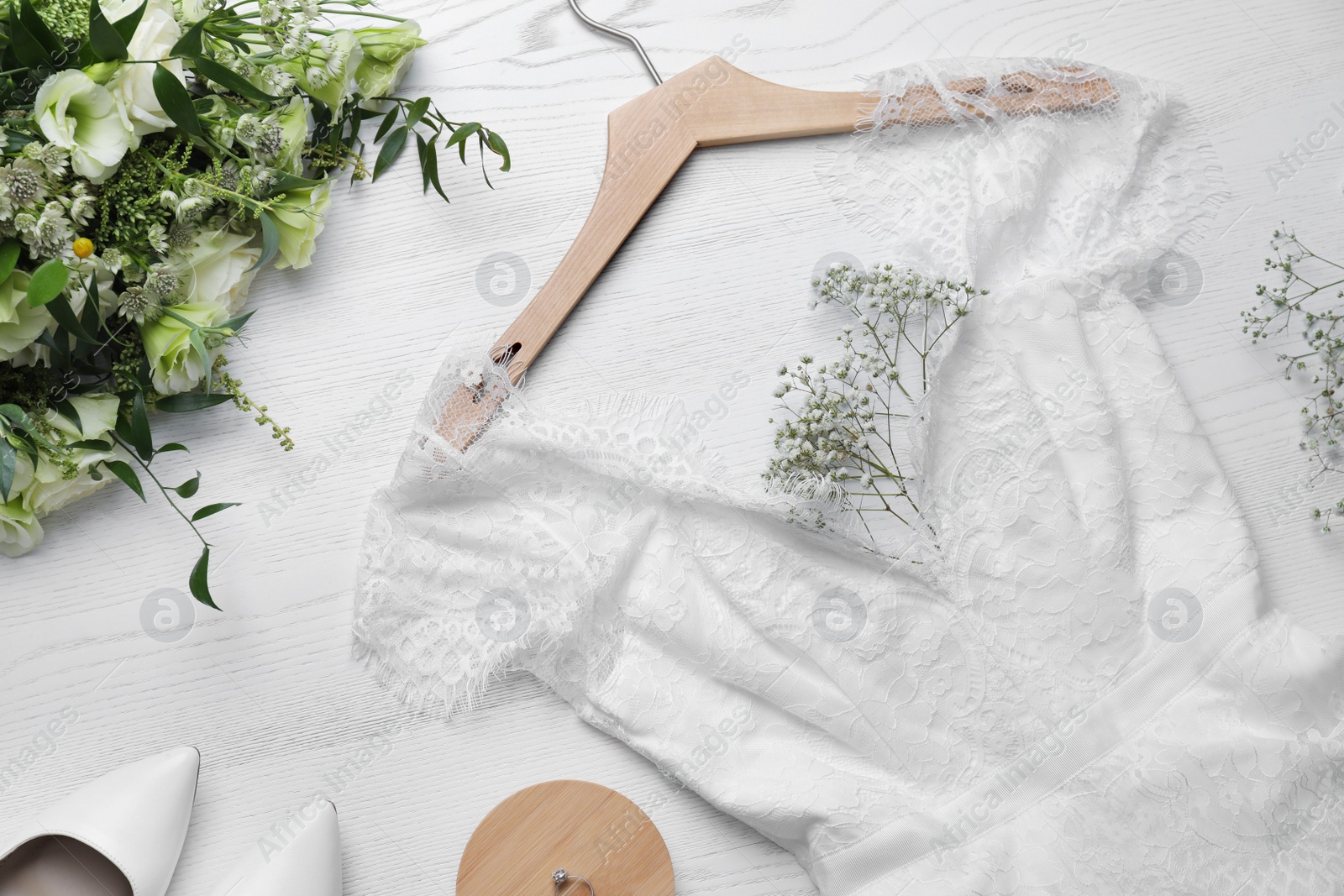 Photo of Beautiful wedding dress, engagement ring and flowers on white wooden background, flat lay