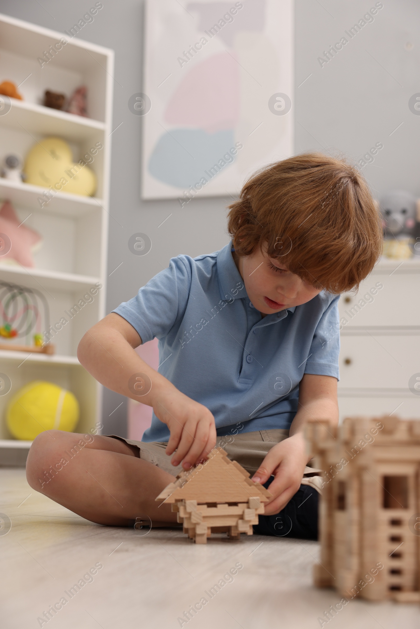 Photo of Little boy playing with wooden construction set on floor in room. Child's toy