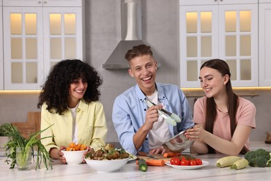 Photo of Friends cooking healthy vegetarian meal at white marble table in kitchen