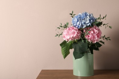 Photo of Beautiful hortensia flowers in can on wooden table against beige background. Space for text