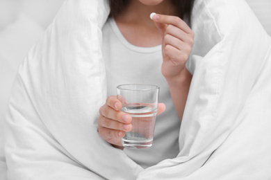 Photo of Woman with glass of water taking pill in bedroom, closeup