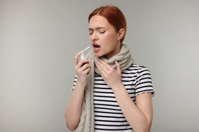 Young woman with scarf using throat spray on grey background