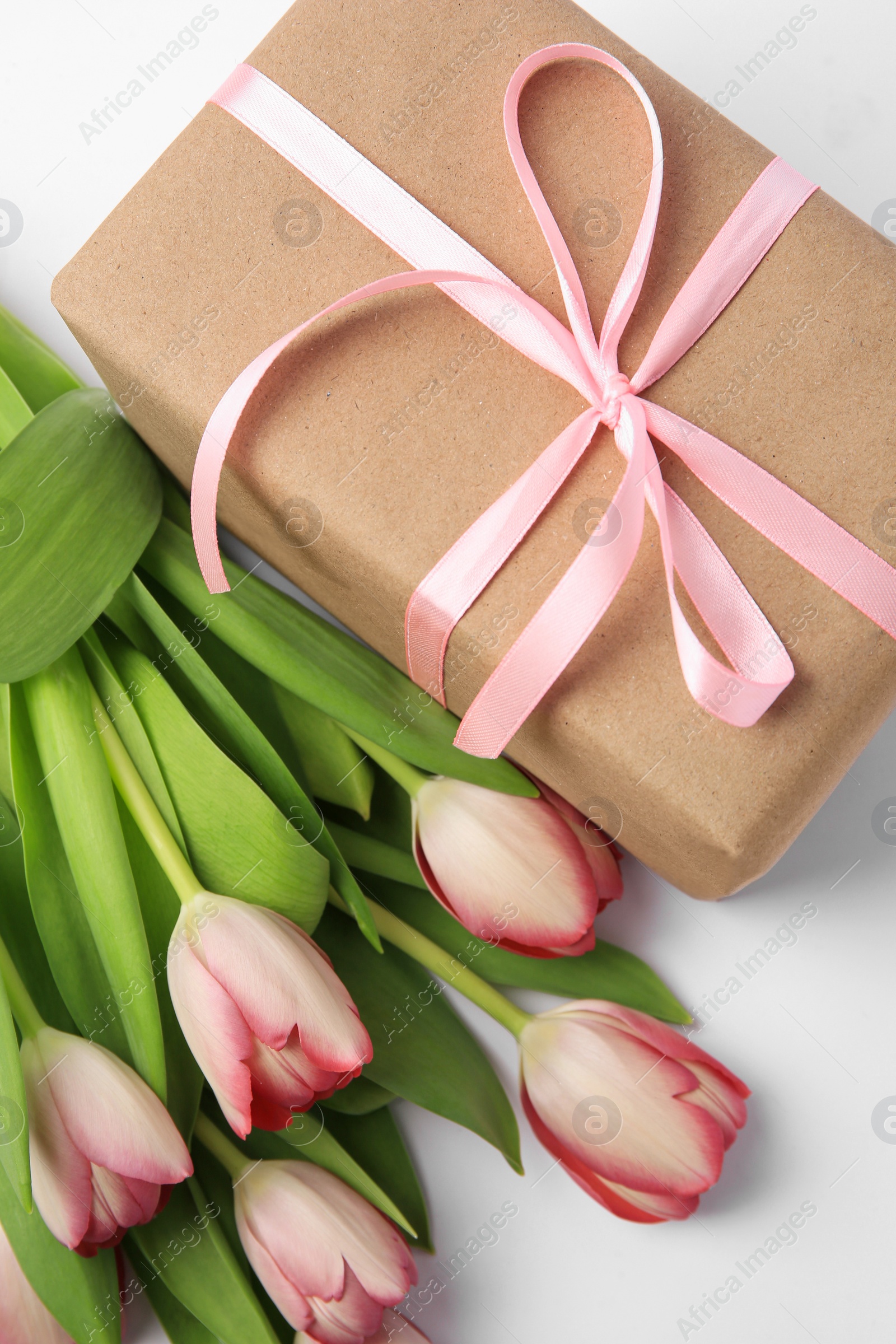 Photo of Beautiful gift box with bow and pink tulips on white background, flat lay