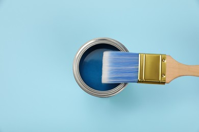 Can of paint and brush on light blue background, top view