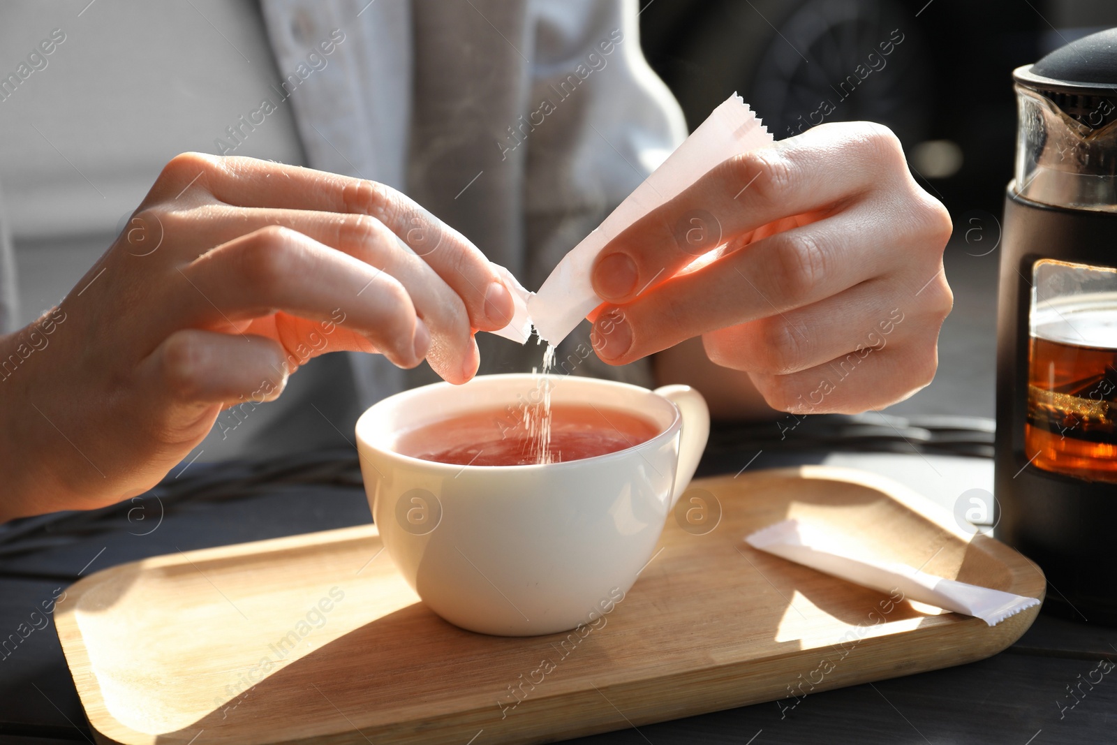 Photo of Woman adding sugar into cup of tea at table, closeup