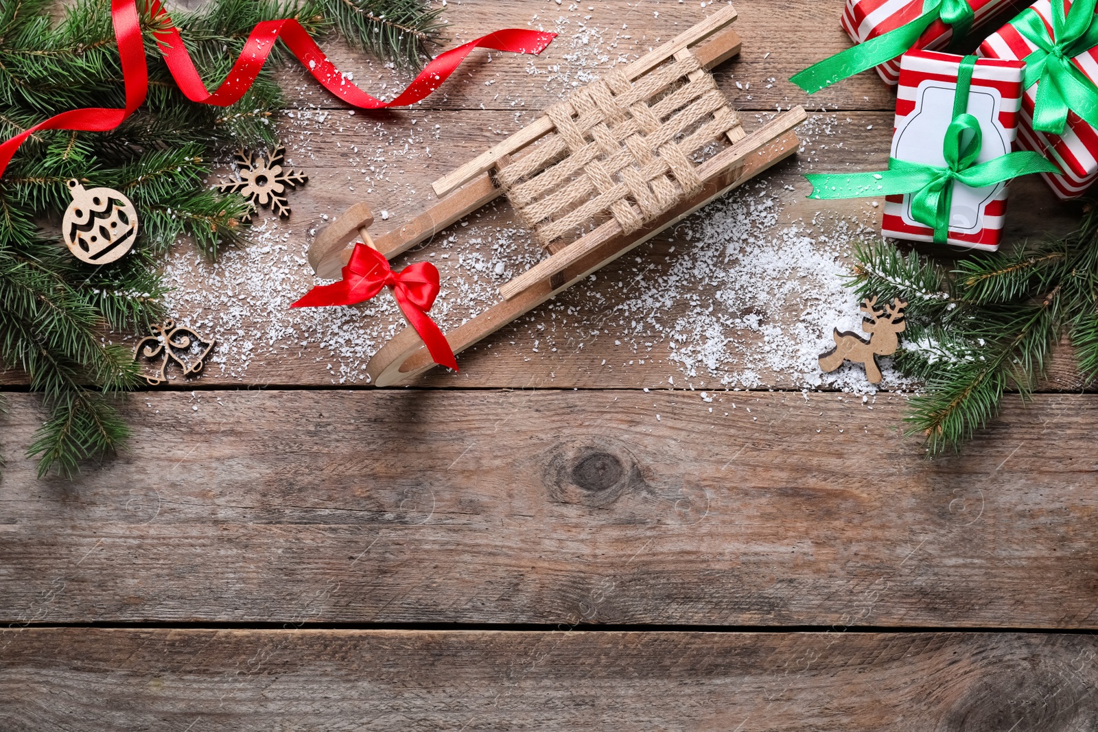 Photo of Flat lay composition with sleigh, fir tree branches and gift boxes on wooden table, space for text