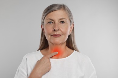 Endocrine system. Senior woman doing thyroid self examination on light grey background