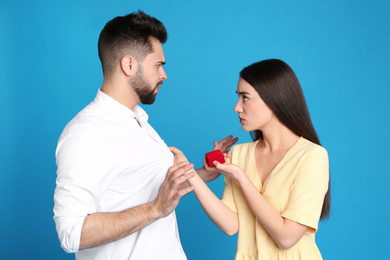 Young man rejecting engagement ring from girlfriend on blue background