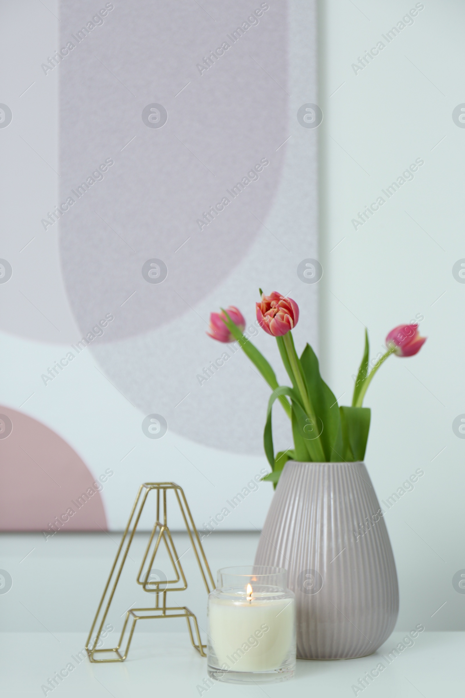 Photo of Vase with beautiful tulips, burning candle and decorative letter on table indoors, space for text. Interior elements