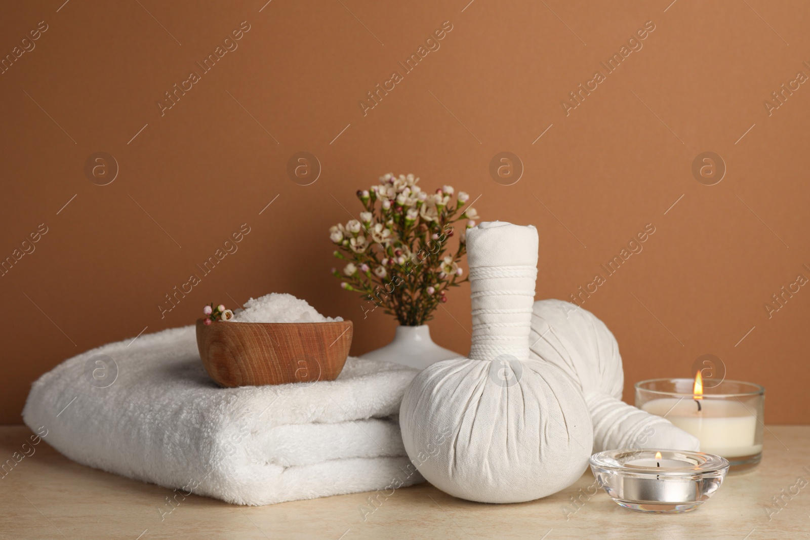 Photo of Composition with different spa products, candles and flowers on beige table against brown background