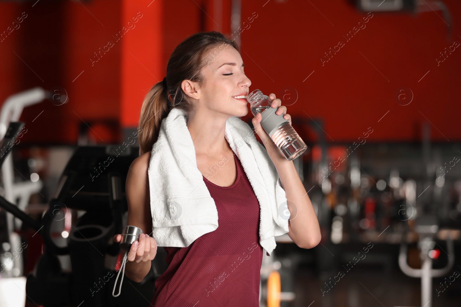 Photo of Beautiful young woman with towel and bottle of water in gym