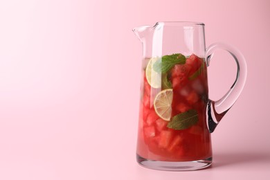 Tasty summer watermelon drink with lime in glass jug on pink background. Space for text