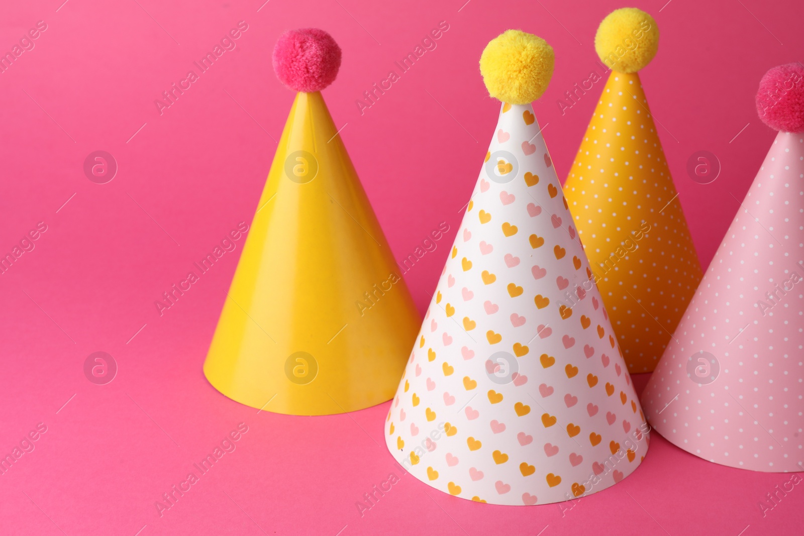 Photo of Beautiful party hats with pompoms on pink background