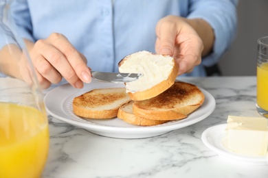 Photo of Woman spreading butter onto slice of bread over marble table, closeup