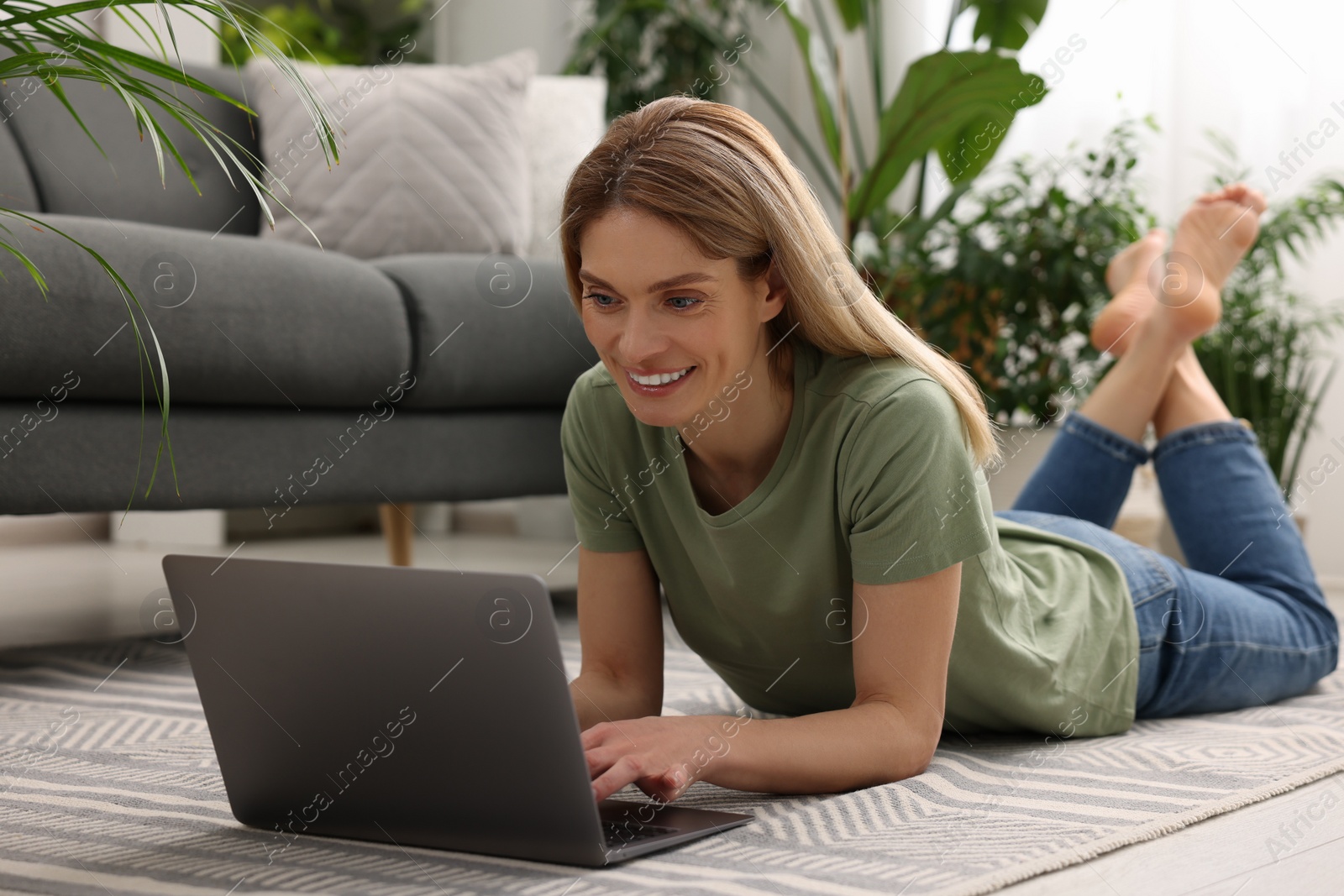 Photo of Woman using laptop on floor in room with beautiful potted houseplants