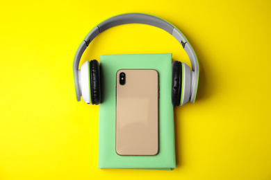 Photo of Book with mobile phone and headphones on yellow background, flat lay