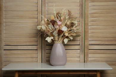 Photo of Beautiful dried flower bouquet in ceramic vase on white table near wooden folding screen