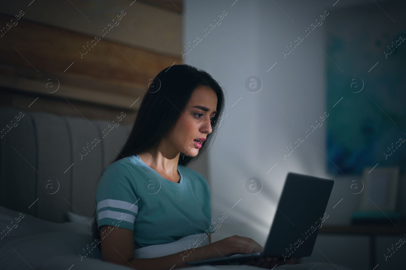 Photo of Emotional young woman with nomophobia using laptop in bed at night. Insomnia concept