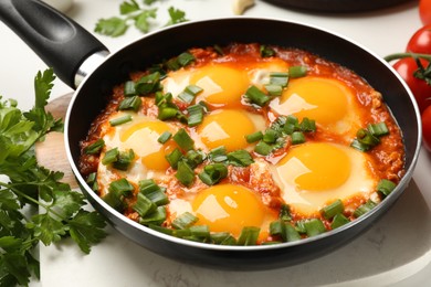 Delicious shakshuka in frying pan on white table, closeup