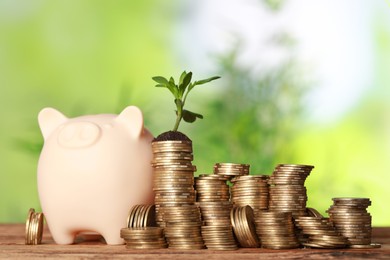 Stacked coins, green sprout and piggy bank on wooden table against blurred background. Investment concept