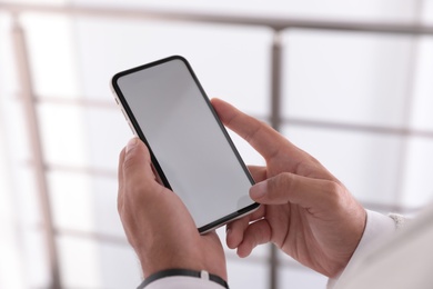 Man holding mobile phone with empty screen indoors, closeup