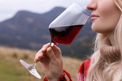 Photo of Young woman drinking wine in peaceful mountains, closeup